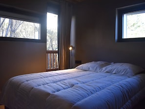 A bedroom with a large bed, two windows, and a nightstand with a lamp. - Apartment panoramic Pyrenees view - guests (Font-Romeu-Odeillo-Via)