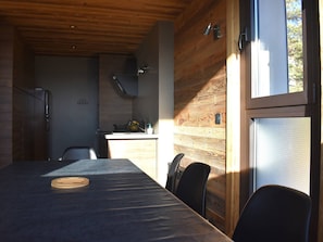 A modern kitchen with wooden walls and a dining area with a table and chairs. - Apartment panoramic Pyrenees view - guests (Font-Romeu-Odeillo-Via)