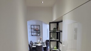 A modern kitchen with a built-in refrigerator, a dining area with a table and chairs, and a hallway with a wooden floor. - ​First-Line Sea View: Luxurious 3-Room Family Apartment – 10 meters from the Water (Jesenice)