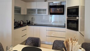 A modern kitchen with a built-in microwave, oven, and a large window above the sink. - ​First-Line Sea View: Luxurious 3-Room Family Apartment – 10 meters from the Water (Jesenice)