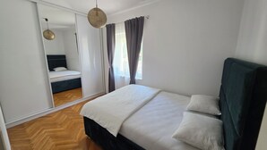 A bedroom with a large bed, a wardrobe, a mirror, and a hanging light fixture. - ​First-Line Sea View: Luxurious 3-Room Family Apartment – 10 meters from the Water (Jesenice)
