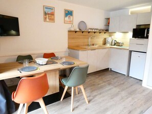 Eine kleine Küche mit Holzarbeitsplatte, einer Spüle und einer Mikrowelle. Es gibt einen Esstisch mit Stühlen und einen an der Wand befestigten Fernseher.