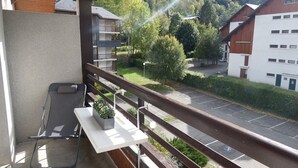 Varanda com vista para um parque de estacionamento e edifícios, uma pequena mesa com uma planta e uma cadeira.