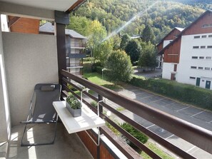 Ein Balkon mit Blick auf einen Parkplatz und Gebäude, ein kleiner Tisch mit einer Pflanze und ein Stuhl.