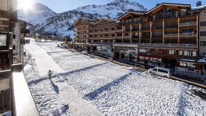 A snow-covered street with a building featuring balconies and a mountain in the background. - Comfortable apartment mountain view - 4 guests (Val-d'Isère)