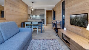 A modern living room with a sofa, a coffee table, and a TV on a wooden wall. - Comfortable apartment mountain view - 4 guests (Val-d'Isère)