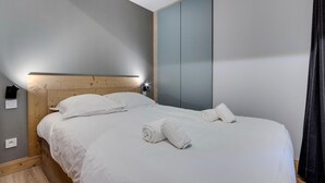 A neatly made bed with white linens and two rolled towels, a wooden headboard, and a wall-mounted light fixture. - Comfortable apartment mountain view - 4 guests (Val-d'Isère)