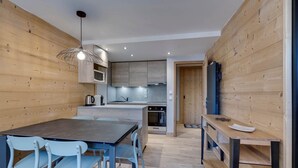A modern kitchen with wooden walls, a central island, and a dining area with blue chairs. - Comfortable apartment mountain view - 4 guests (Val-d'Isère)