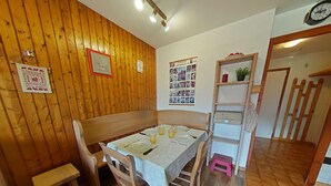 Zona pranzo con tavolo di legno apparecchiata per due persone, una panca e uno scaffale con una pianta.