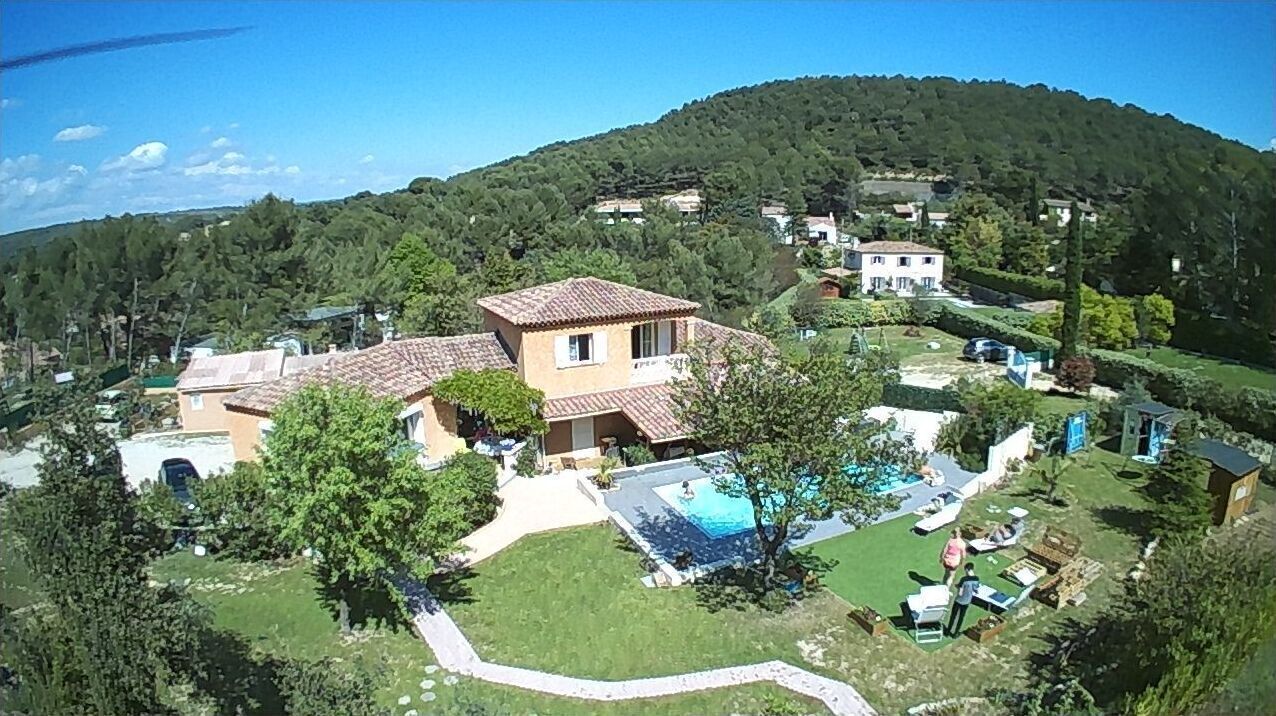 Ein Wohnhaus mit Pool, einem großen Gebäude und hügeliger Landschaft im Hintergrund.