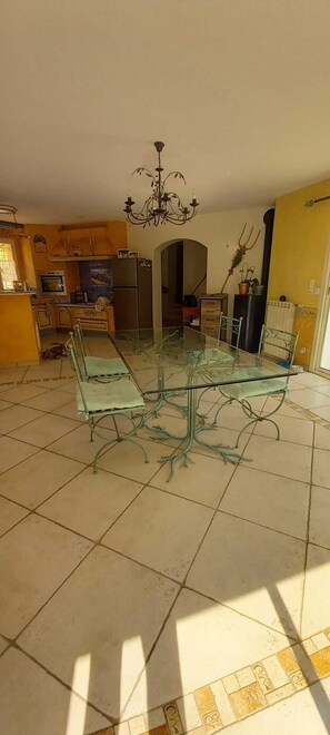 A dining area with a glass table and metal chairs, a kitchen in the background, and a chandelier. - Air-conditioned Provençal villa with a pool (8 m x 4 m)—a haven of peace.... (Ventabren)