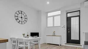 Eine moderne Küche mit weißer Arbeitsplatte, einem Esstisch mit Stühlen, einer schwarzen Uhr und einem Fenster mit Jalousien.