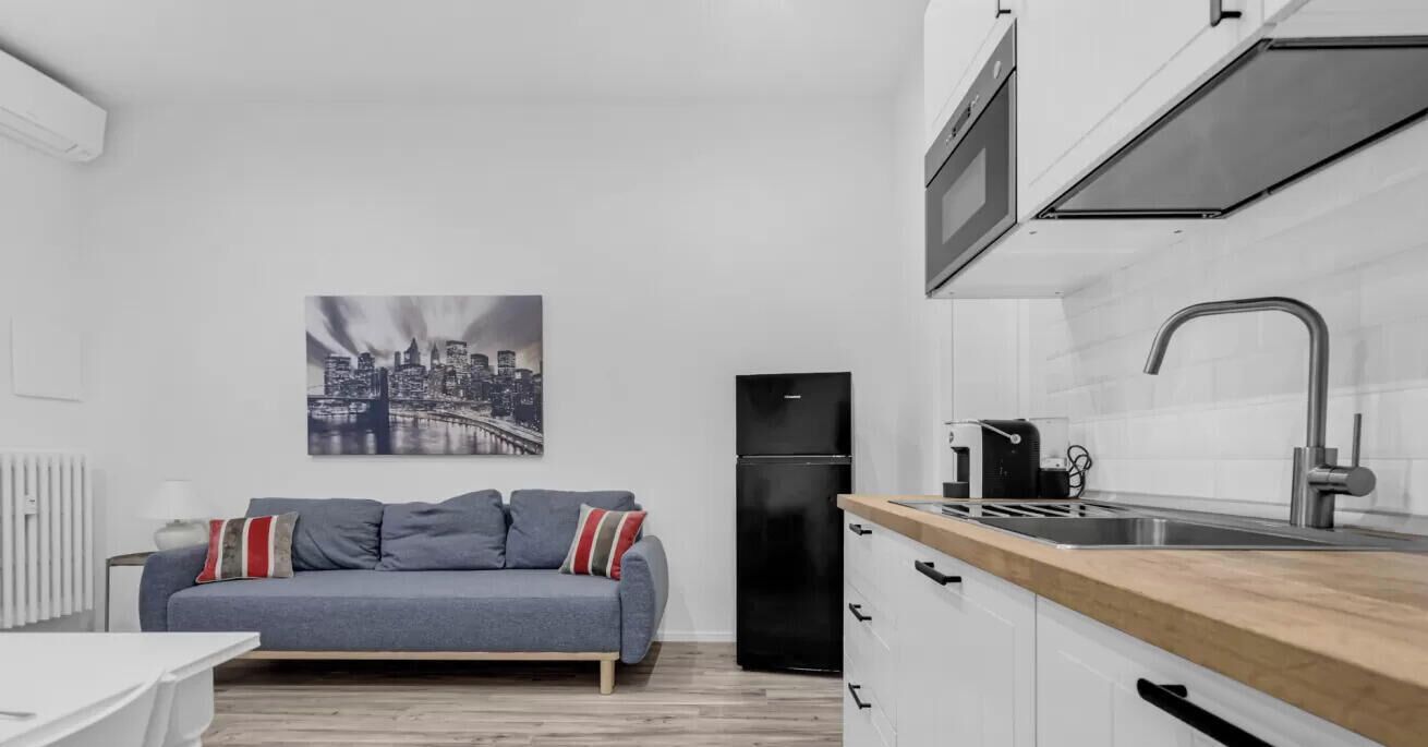 A compact kitchen with a refrigerator, sink, and a cityscape painting on the wall.