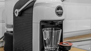 Eine Kaffeemaschine mit einem Glasbecherhalter, einem Wasserbehälter und einem Markenlogo.