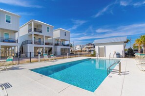 Uma área de piscina com uma piscina azul límpida, edifícios brancos com varandas e um deck cercado com espreguiçadeiras.