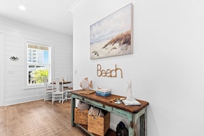 Ein küsteninspiriertes Interieur mit einem Holztisch, Korbwannen und einem Gemälde vom Strand.