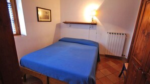 A bedroom with a bed, a wall-mounted shelf with a lamp, a radiator, and a wooden door.