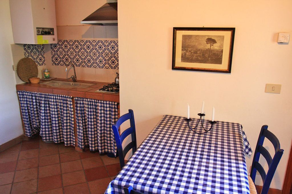 A kitchen with a tiled backsplash, a framed picture on the wall, and a checkered tablecloth-covered table with candles.