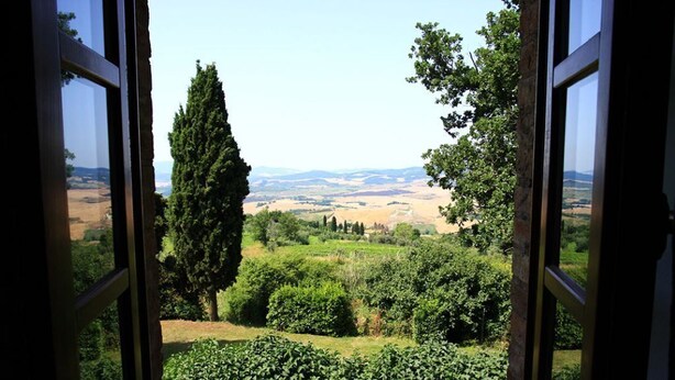 An open window with a view of a lush garden and distant hills.