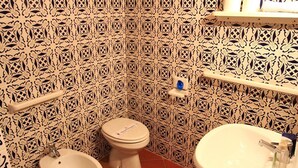 A bathroom with a toilet, bidet, and sink, all with a decorative patterned wall.