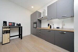 A modern kitchen with grey cabinets, a wooden countertop, a built-in oven, and a coffee machine. - 4BNB - Luxury Chinotto Apartment (Roma)