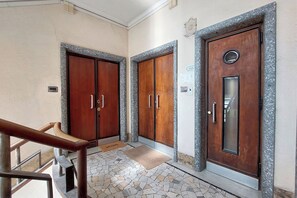 Un pasillo con dos puertas de madera, una barandilla de metal y suelo de baldosas.