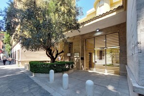 A building with a large tree in front, a gated entrance, and a clear sky. - 4BNB - Luxury Chinotto Apartment (Roma)