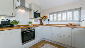 A modern kitchen with white cabinets, a built-in oven, a microwave, and a window with blinds. - Penrallt - sleeps 8 guests  in 4 bedrooms (Benllech)