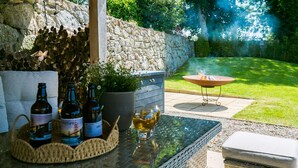 An outdoor patio with a stone wall, a fire pit, and a table with bottles and glasses. - Penrallt - sleeps 8 guests  in 4 bedrooms (Benllech)