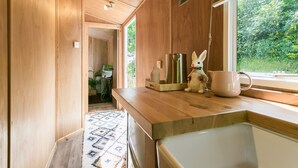 A kitchen with wooden cabinets, a sink, a window, and a small rabbit figurine on the counter. - Penrallt - sleeps 8 guests  in 4 bedrooms (Benllech)