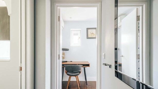A hallway leading to a room with a desk, chair, and framed picture on the wall. - The Knaresborough -Stylish Earl's Court Apartment (London)