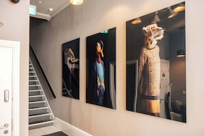A hallway with a staircase, three framed artworks on the wall, and a door. - The Knaresborough -Stylish Earl's Court Apartment (London)