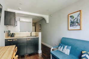 A compact kitchen with a built-in stove, a sink, and a dining area with a wooden table and chairs. - The Knaresborough by nestor - Earl's Court Apt. (London)