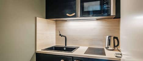 A compact kitchen with a built-in microwave, a kettle, and a sink.