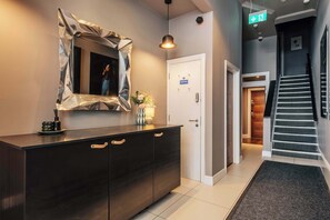 Eine moderne Hotelhalle mit dunklem Holzboden, einer Rezeption mit dunklem Holzboden, einem Spiegel mit geometrischer Umrandung, einer Treppe und einer Tür mit der Aufschrift 'Personal Only'.