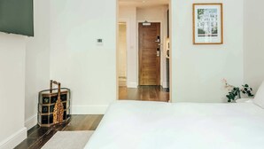 Ein Hotelzimmer mit einem Bett, einer Holztür, einem gerahmten Bild und einem kleinen Tisch mit einer Pflanze.