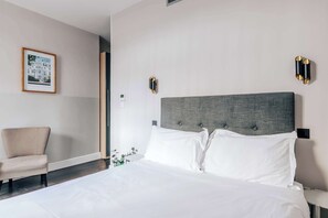 Quarto de hotel com uma cama grande, uma cadeira e um quadro na parede.