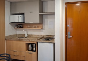 A compact kitchen with a microwave, coffee maker, and a small refrigerator. - SHB Azul Infinito Sua Janela para o Mar (Santos)
