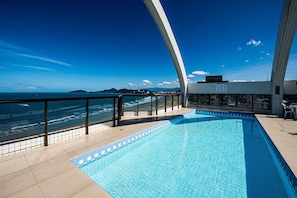 A swimming pool with a view of the ocean, a glass balustrade, and a tiled building. - SHB Azul Infinito Sua Janela para o Mar (Santos)