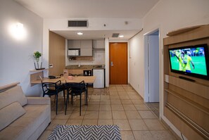 A modern living room with a sofa, dining table, chairs, a TV, and a kitchen in the background. - SHB Azul Infinito Sua Janela para o Mar (Santos)