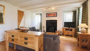 A living room with a wooden coffee table, a sofa, a fireplace, and a television. - Cornwall Cottage - Sleeps 6 - Garden - Pets (Bodmin)