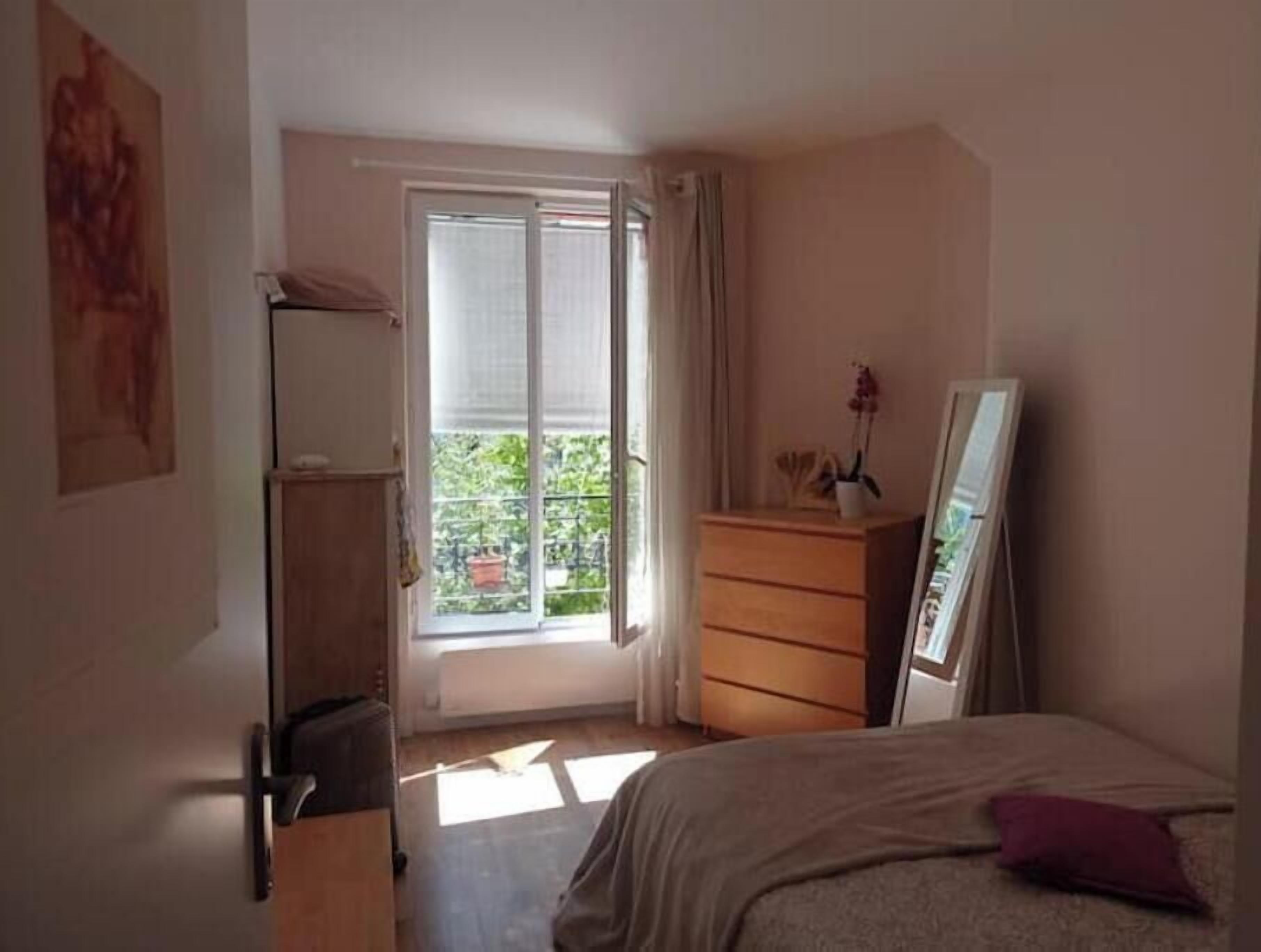 Ein Schlafzimmer mit Bett, Kommode, Fenster mit Vorhängen und Tür.