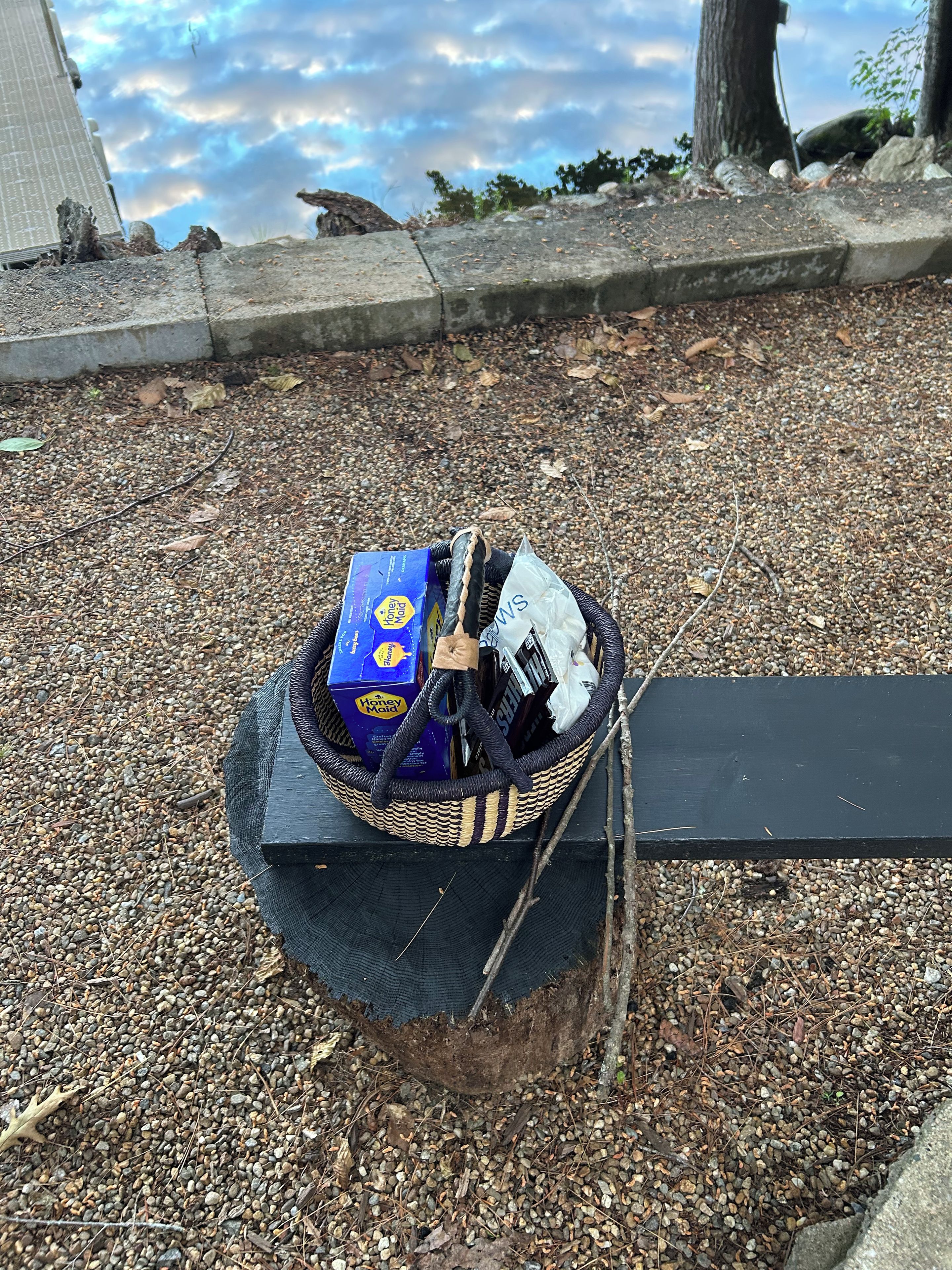 Un panier en osier rempli d’objets, posé sur une surface de gravier.