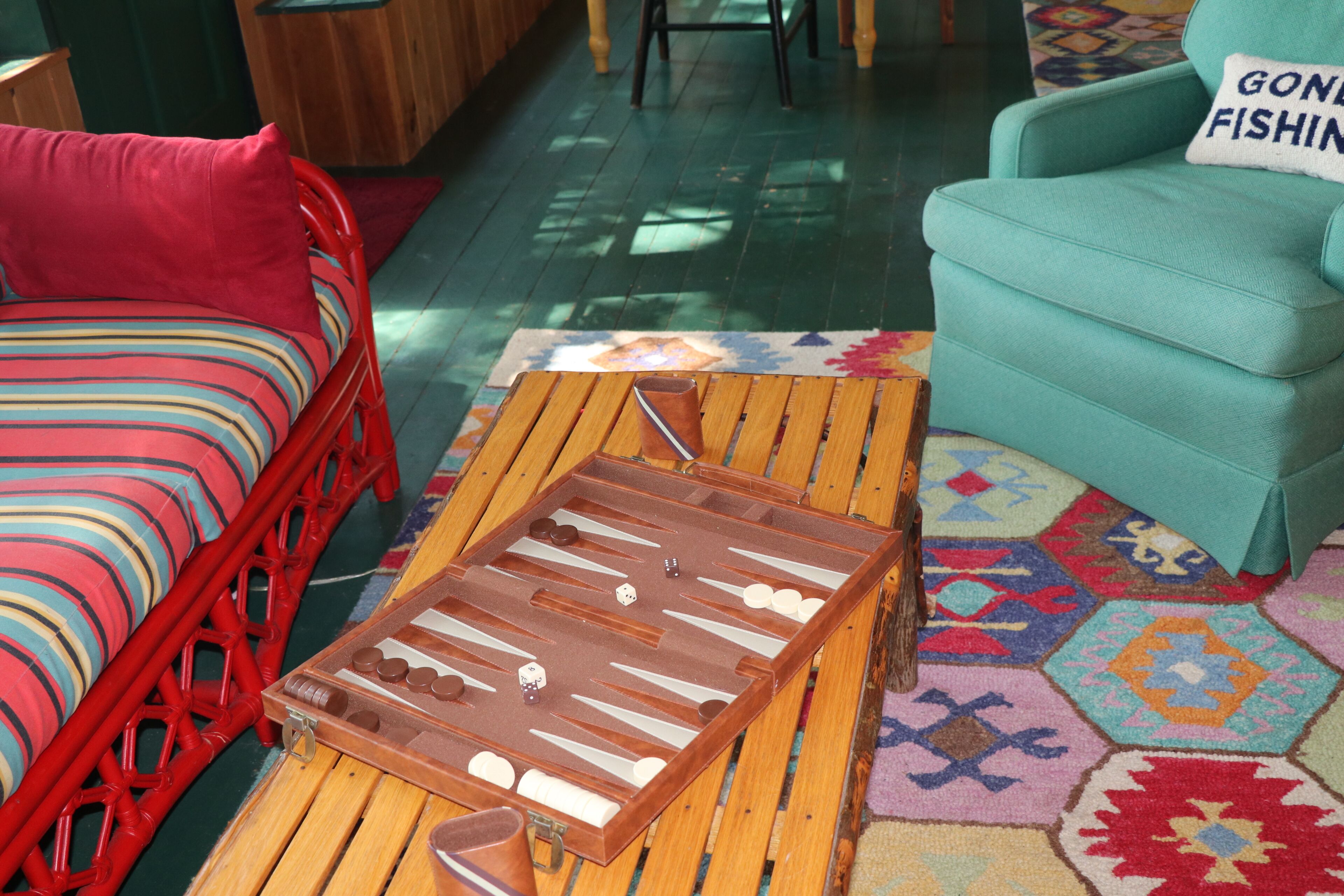Una habitación con una mesa de centro de madera, una silla roja, un sillón verde azulado y una alfombra colorida.