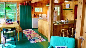 A cozy cabin interior with a wooden dining table, chairs, a kitchen area, and a colorful rug.