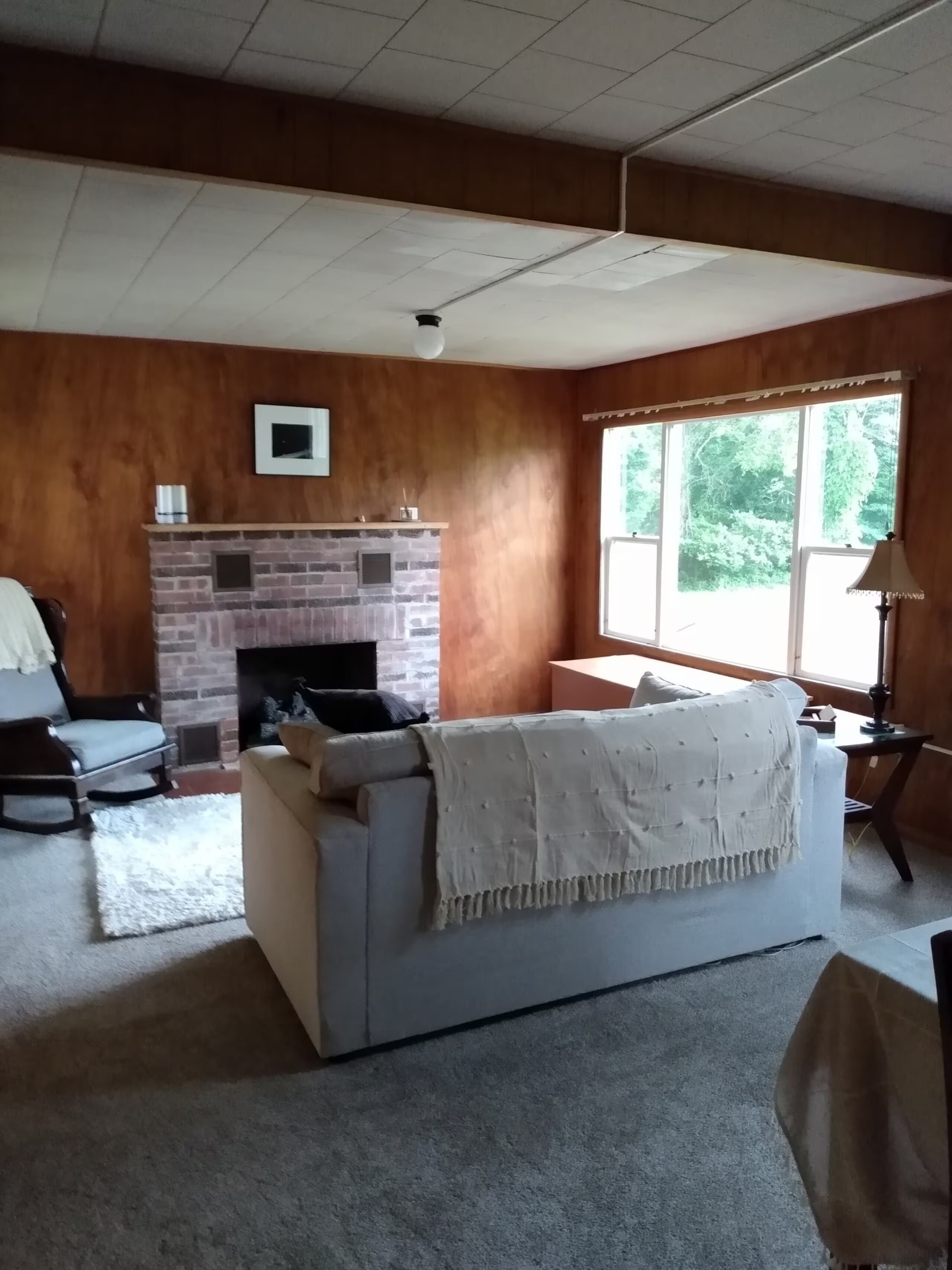 A living room with a fireplace, a sofa, a chair, and a large window.