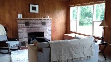 A living room with a fireplace, a sofa, a chair, and a large window.
