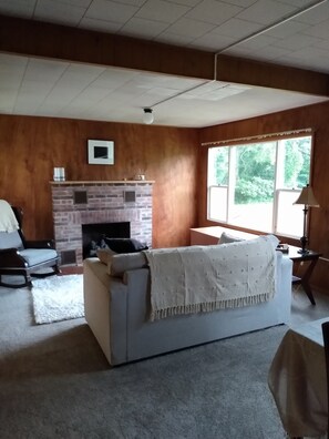 Ein Wohnzimmer mit Kamin, einer Couch, einem Sessel und einem großen Fenster.