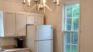 A kitchen with white cabinets, a white refrigerator, a wooden island, two stools, and a chandelier.