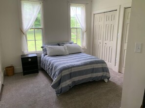A bedroom with a bed, a nightstand, a dresser, a window with curtains, and a door.